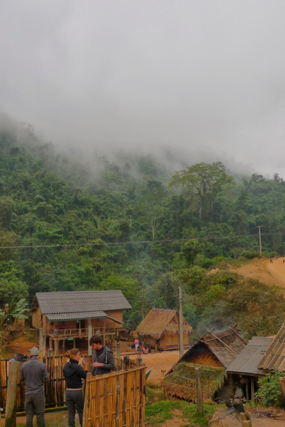 Early morning on day 2 of trekking: fog crawls over the mountain walls that surround us. In the foreground, the bamboo structure you can glimpse is the communal village shower where everyone washes, covered in sarongs for modesty.